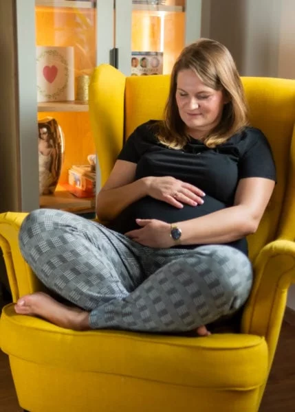 fotografia ciążowa łódź sesja ciążowa w domu kobieta siedzi na fotelu i spogląda na swój brzuch r 02