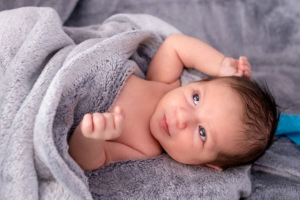 sesja noworodkowa w domu łódź noworodek leży na plecach z ręką opartą na głowie i uśmiecha się k15